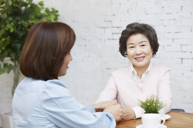 모녀가 테이블이 있는 의자에 앉아있고, 딸은 옆모습이 보이고, 어머니의 웃는 모습이 정면으로 보이는 사진입니다.