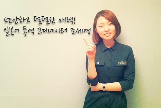 벽에 기대 선 단발머리의 여직원이 미소지며 서 있다.